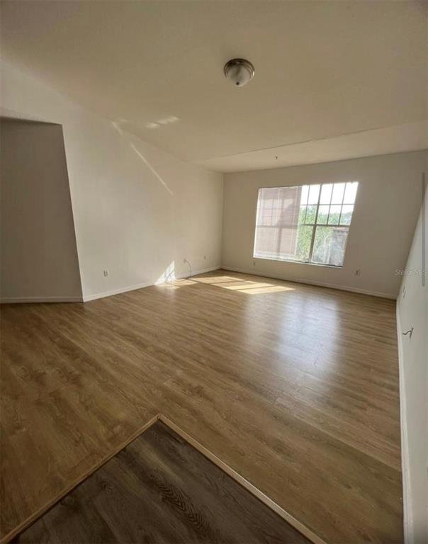 An empty room features light wood-look flooring, white walls, and a large window — 5548 METROWEST BOULEVARD UNIT 306, ORLANDO, FL