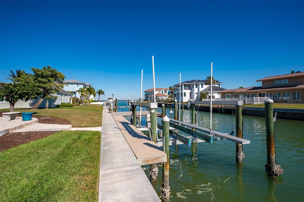 A concrete dock with a boat lift extends into a canal beside a grassy yard — 548 GUNWALE LANE, LONGBOAT KEY, FL