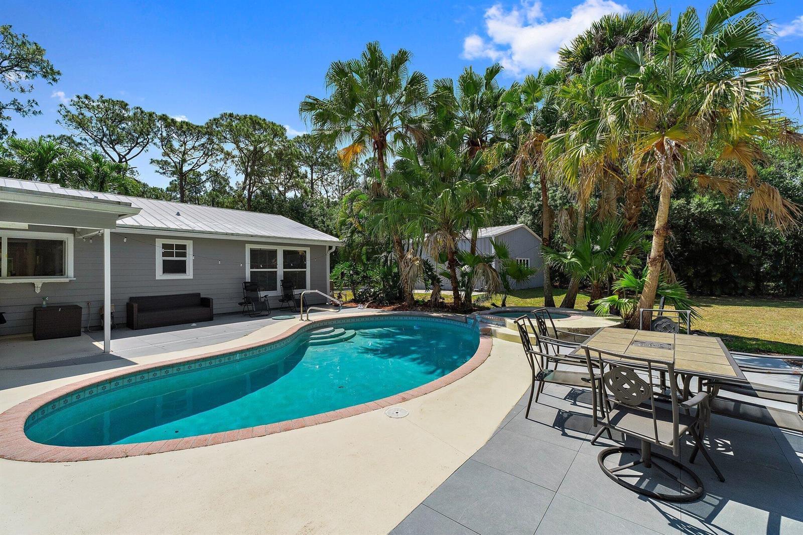 A backyard features a kidney-shaped swimming pool, a patio dining set, and palm trees — 11217 169th Court N, Jupiter FL 33478, JUPITER, FL