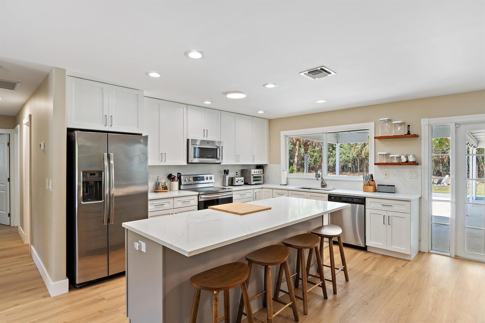 A modern kitchen features white cabinetry, stainless steel appliances, a central island, and wood flooring — 11217 169th Court N, Jupiter FL 33478, JUPITER, FL