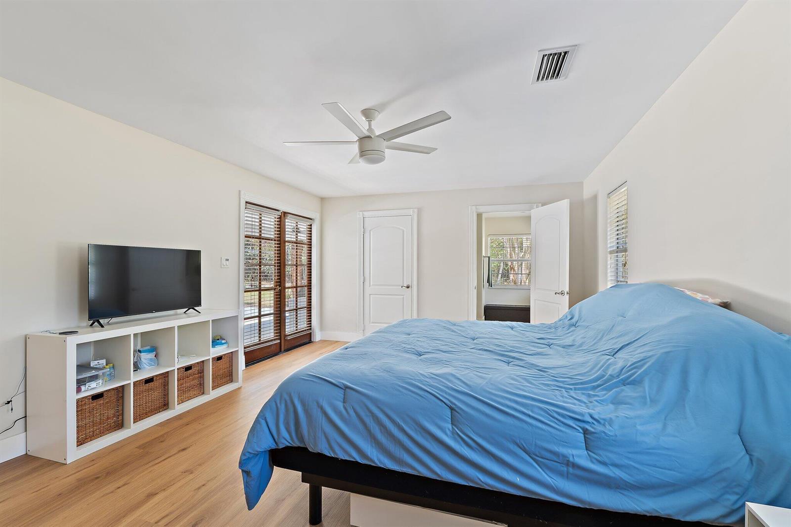 A bedroom with light wood flooring, a blue bedspread, a white media console, and French doors — 11217 169th Court N, Jupiter FL 33478, JUPITER, FL