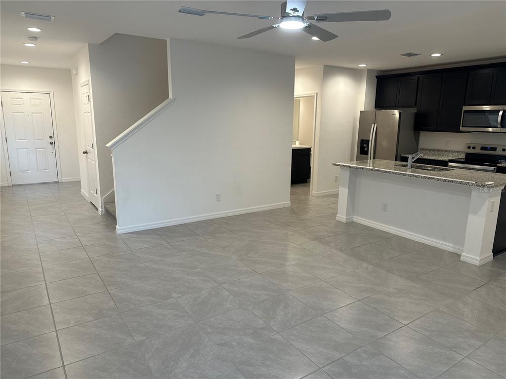 An open-concept living area features gray tile flooring, a kitchen with dark cabinets, and stairs — 189 GLASS ONION DRIVE, HOWEY IN THE HILLS, FL