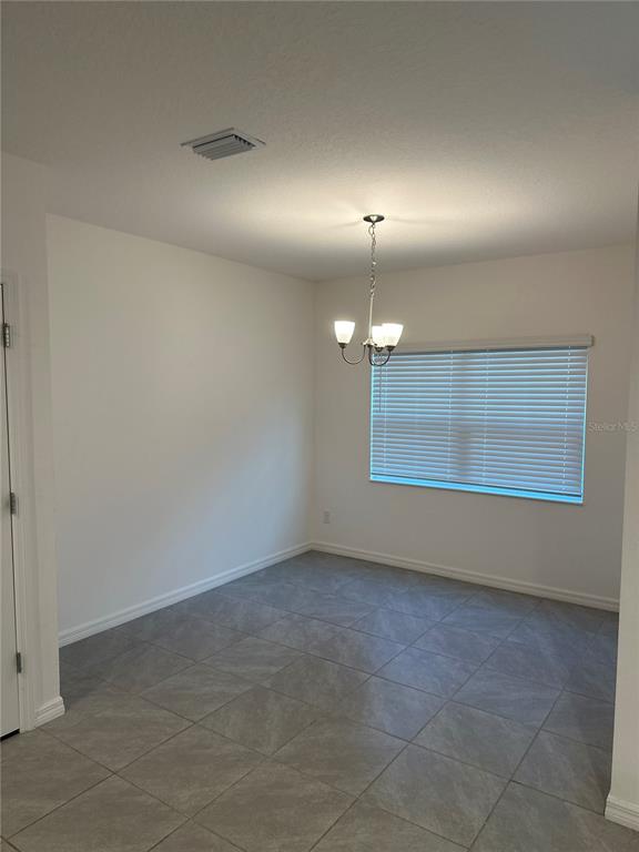 A dining area features gray tile flooring, a chandelier, and a window with white blinds — 189 GLASS ONION DRIVE, HOWEY IN THE HILLS, FL