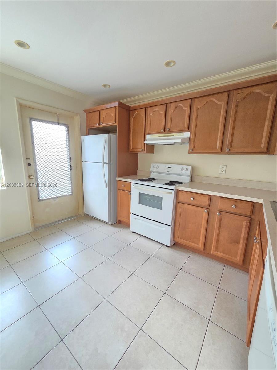 A kitchen features wooden cabinets, white appliances, and light-colored tile flooring — 1000 NE 14th Ave # 210, Hallandale Beach FL 33009, HALLANDALE BEACH, FL