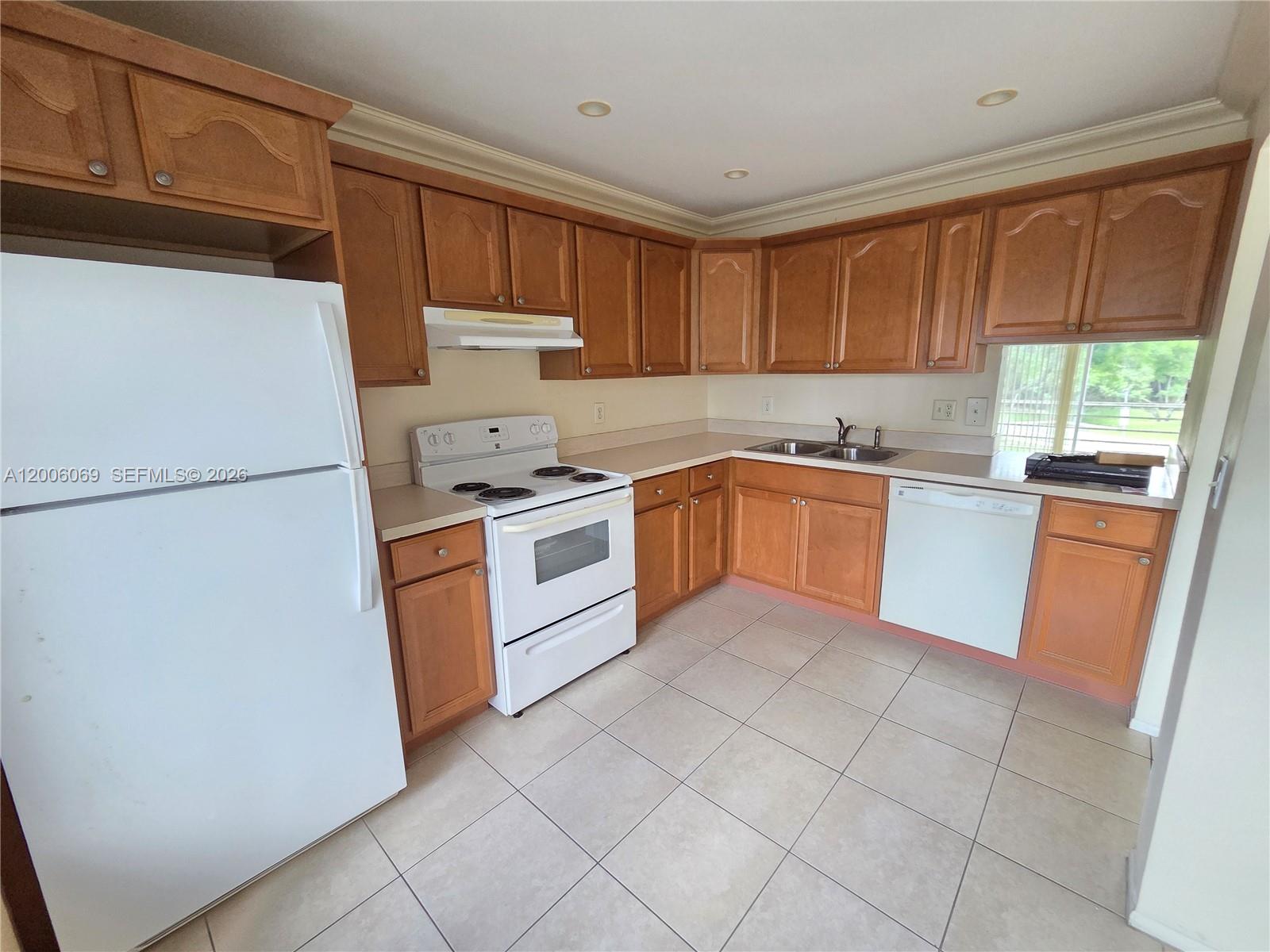 A kitchen features wood cabinets, white appliances, beige tile flooring, and a double sink — 1000 NE 14th Ave # 210, Hallandale Beach FL 33009, HALLANDALE BEACH, FL