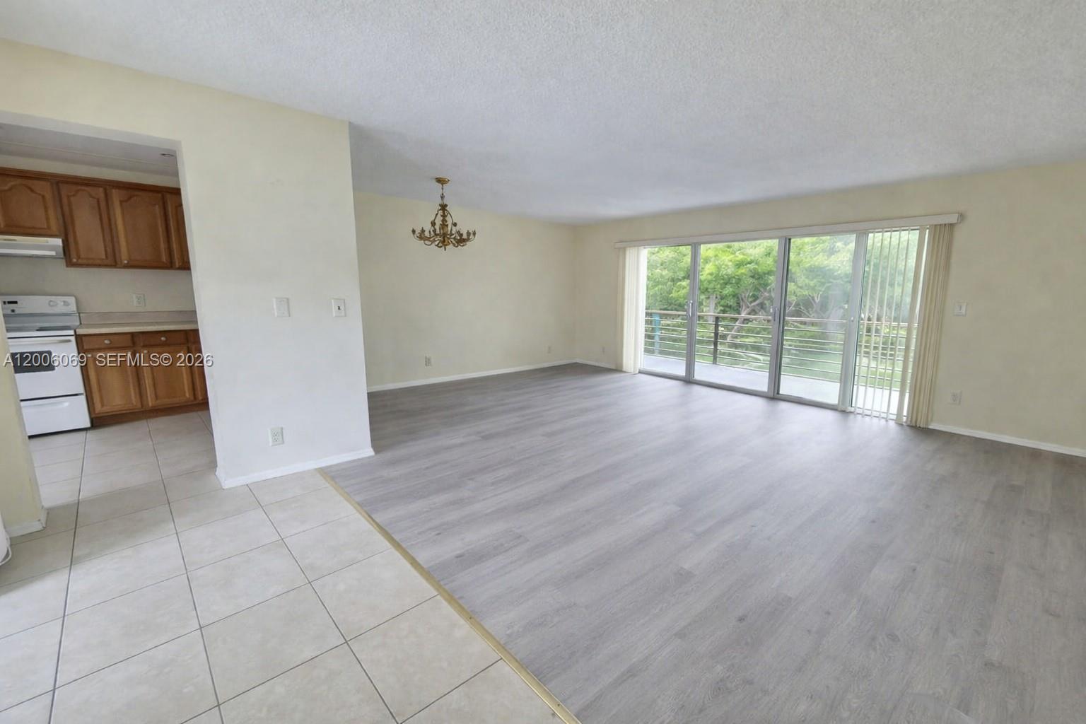This living room features gray wood-look flooring, a chandelier, and sliding glass doors to a balcony — 1000 NE 14th Ave # 210, Hallandale Beach FL 33009, HALLANDALE BEACH, FL