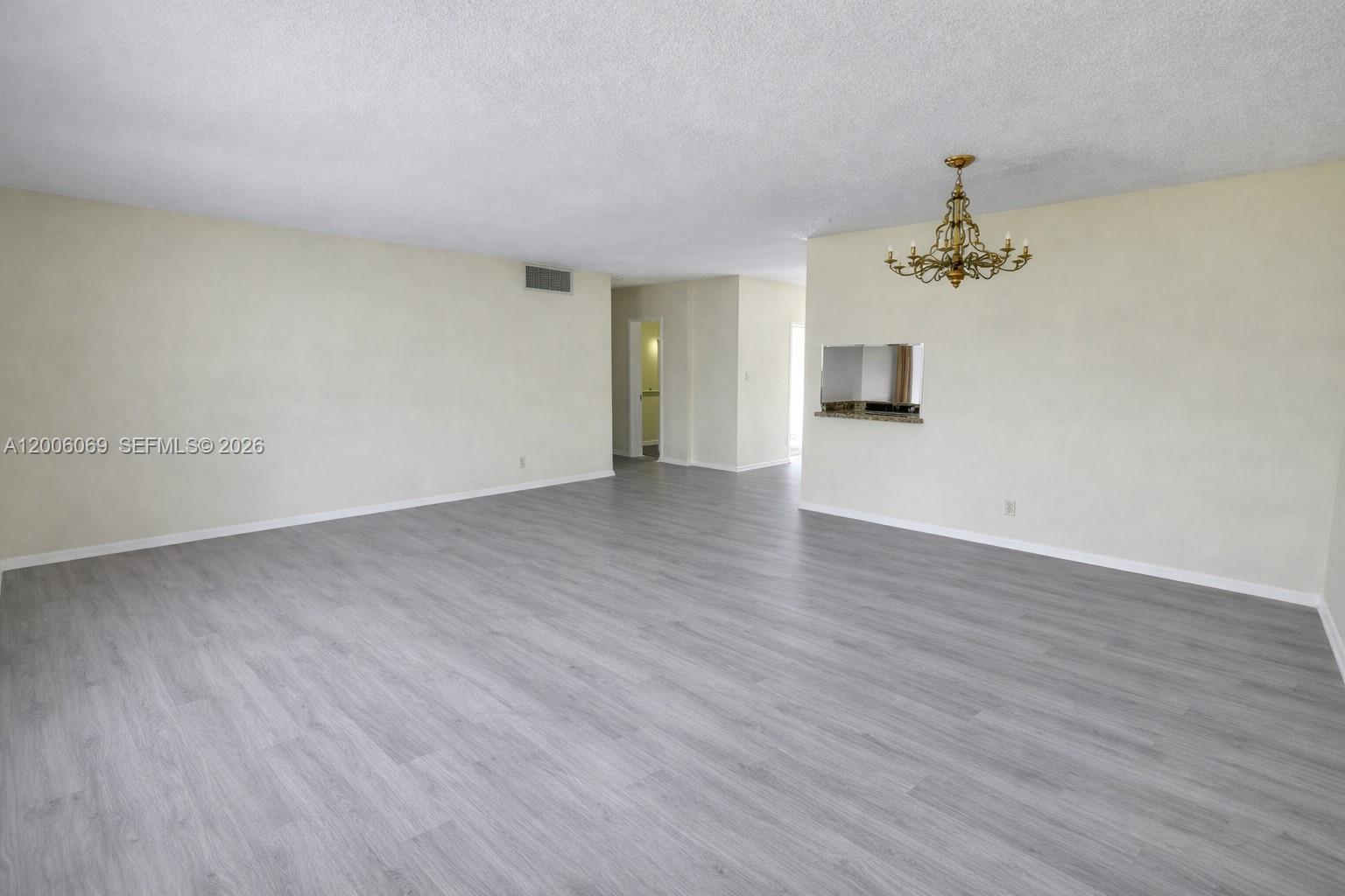 An empty living room features light gray wood-look flooring, beige walls, and a brass chandelier — 1000 NE 14th Ave # 210, Hallandale Beach FL 33009, HALLANDALE BEACH, FL