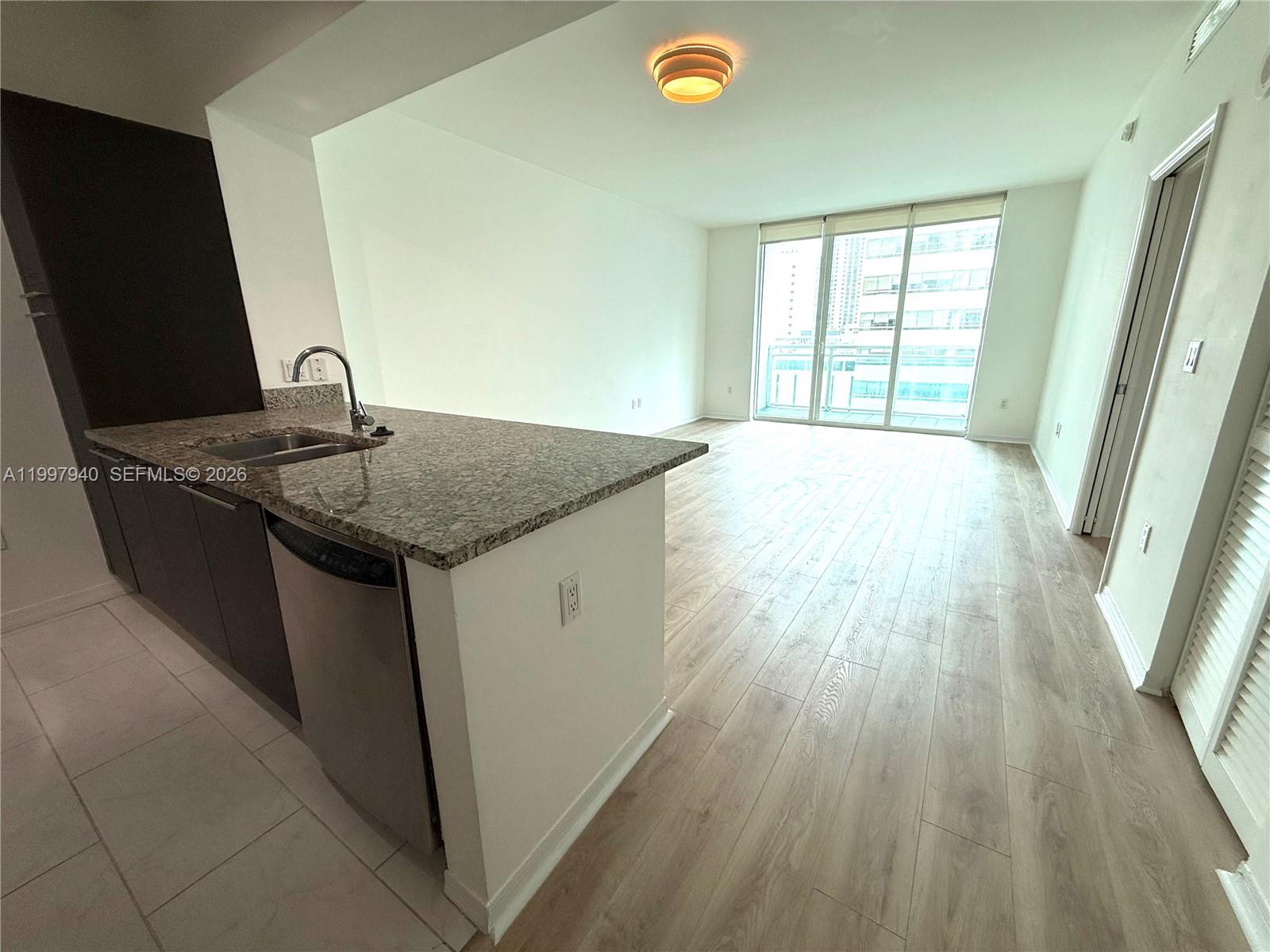 A kitchen with granite countertops and stainless steel appliances opens into a bright living area — 951 Brickell Ave # 1103, Miami FL 33131, MIAMI, FL