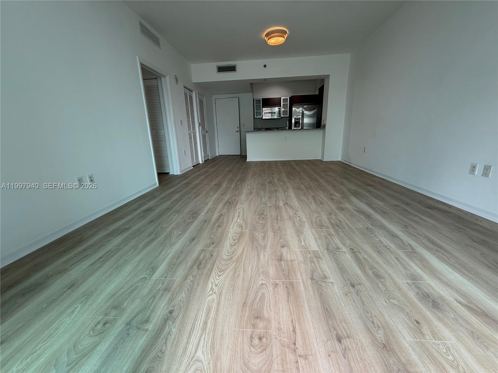 An empty living area features light wood-look flooring, white walls, and an open kitchen — 951 Brickell Ave # 1103, Miami FL 33131, MIAMI, FL