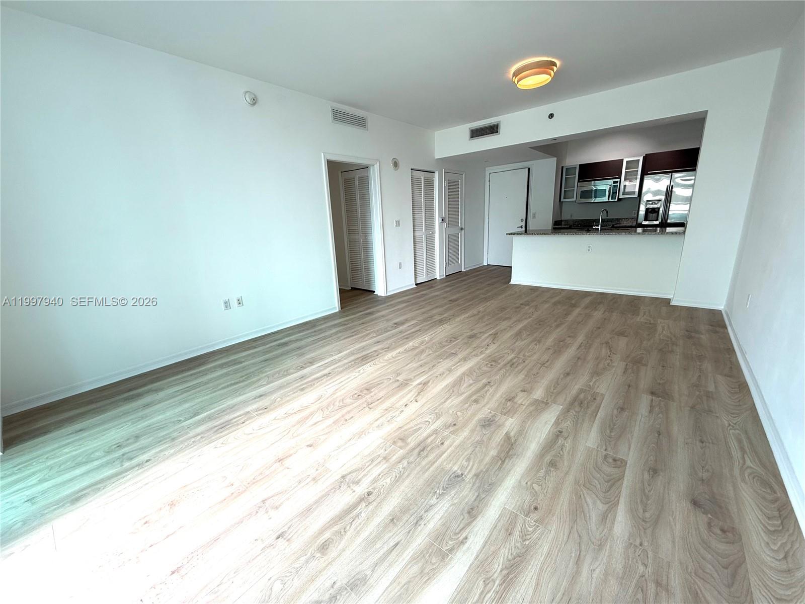 An open-concept living area features light wood-look flooring, white walls, and an adjacent kitchen — 951 Brickell Ave # 1103, Miami FL 33131, MIAMI, FL