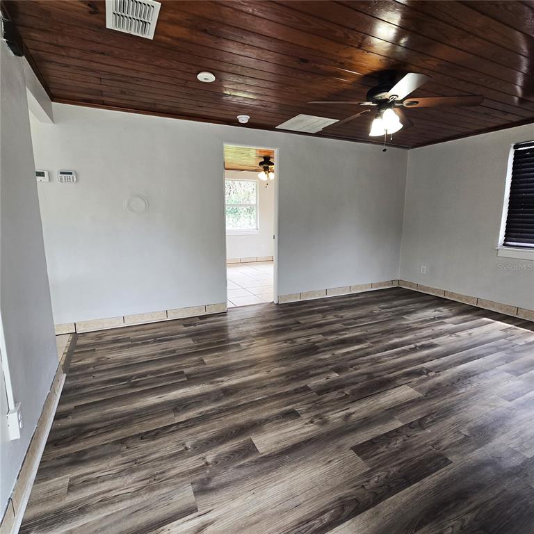 A living room with wood-plank ceiling, dark wood-look flooring, and a doorway to another room — 2710 AVENUE J NW, WINTER HAVEN, FL