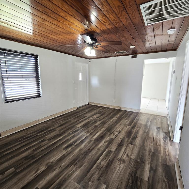 A room with wood-paneled ceiling, ceiling fan, dark wood-look flooring, and a white door — 2710 AVENUE J NW, WINTER HAVEN, FL