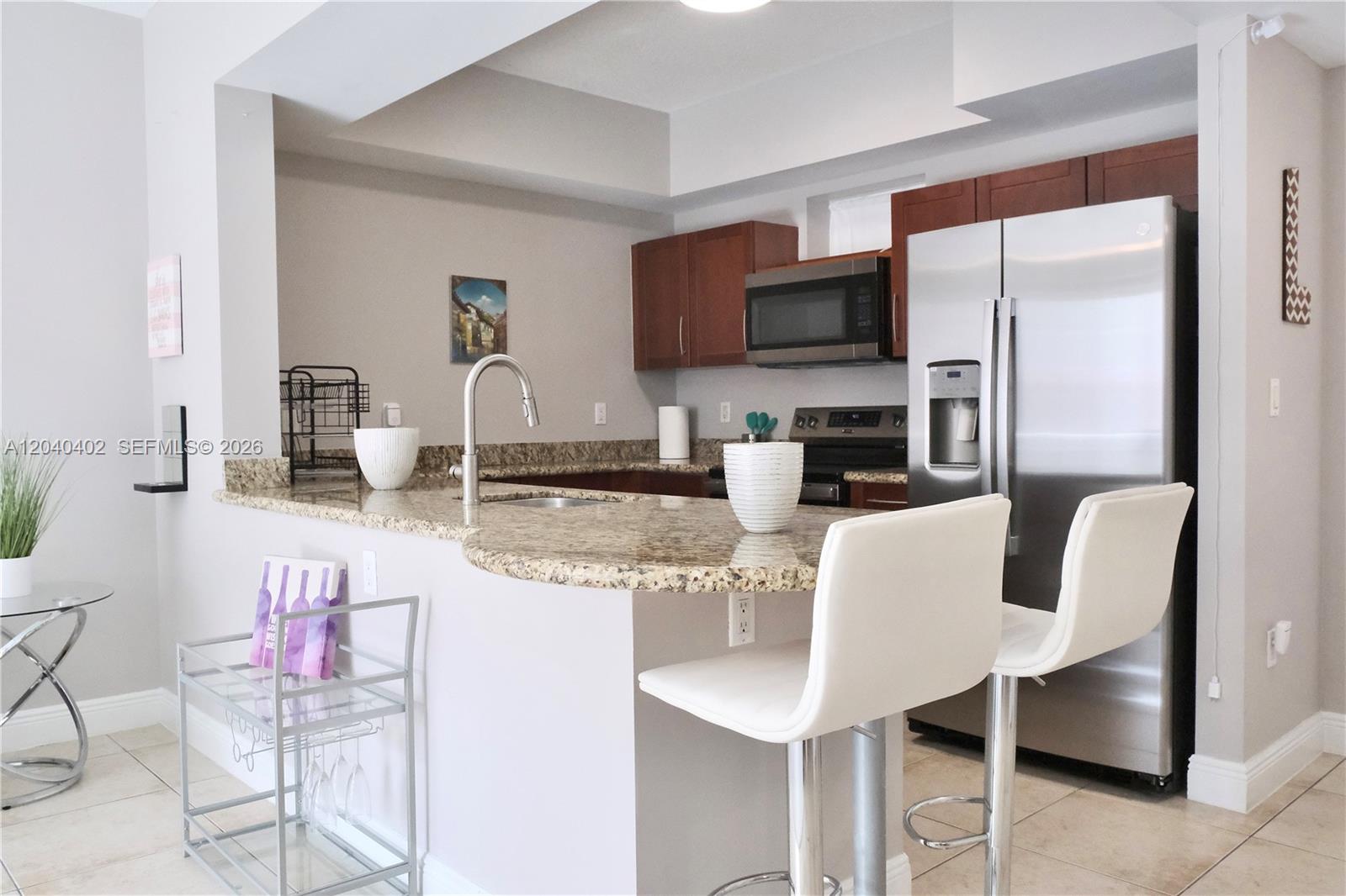 A kitchen features a granite breakfast bar, stainless steel appliances, and white bar stools — 7275 SW 90th St # C409, Miami FL 33156, MIAMI, FL