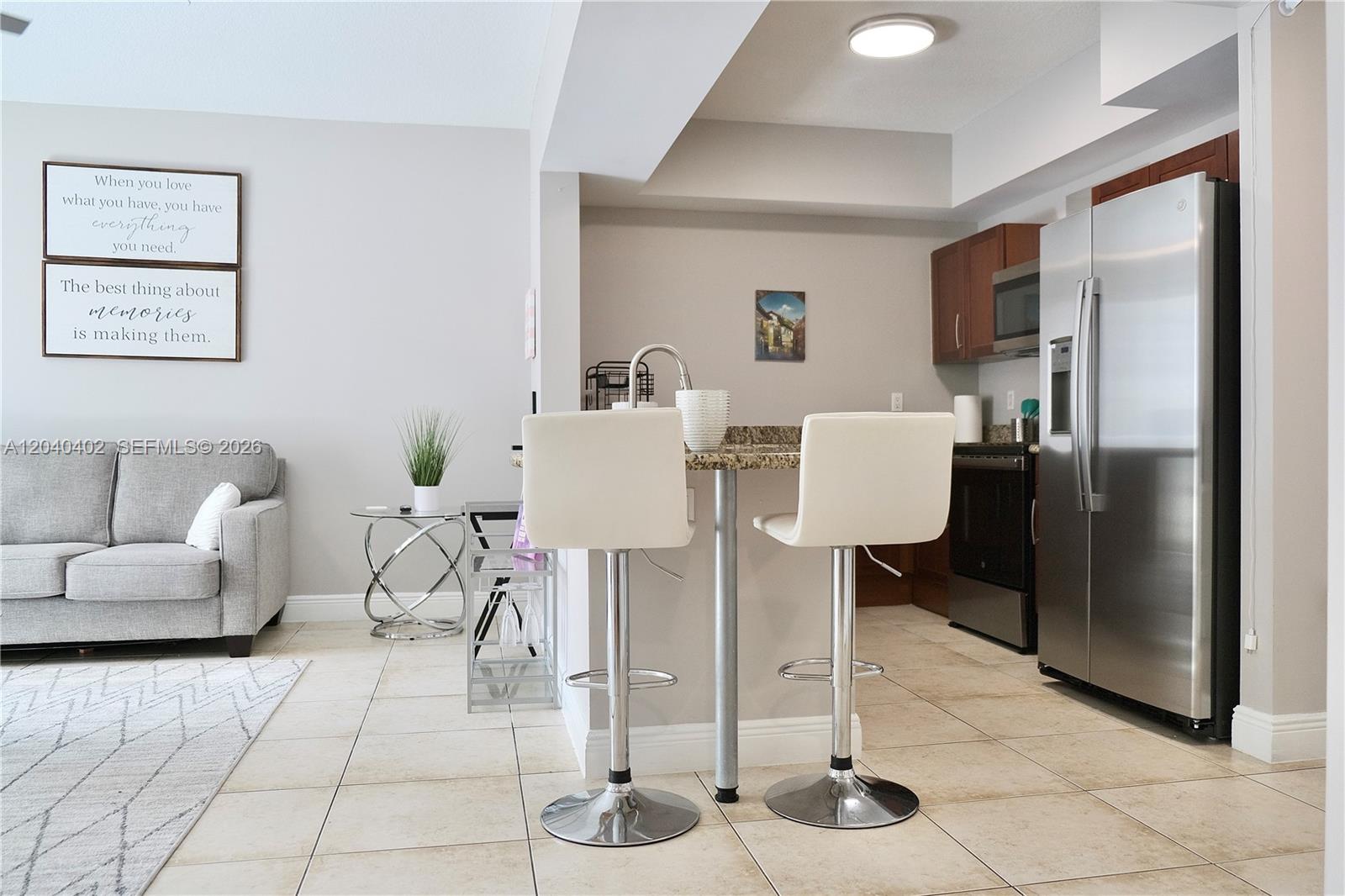 A kitchen with stainless steel appliances and a breakfast bar faces a living area — 7275 SW 90th St # C409, Miami FL 33156, MIAMI, FL