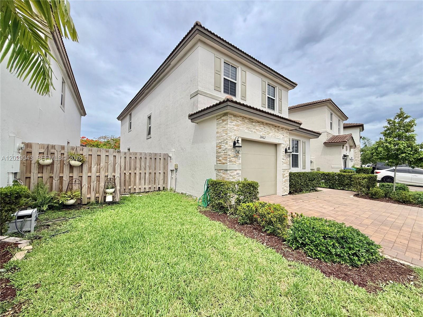A two-story house with a stone-accented garage, a paved driveway, and a wooden fence — 2462 NW 131st Cir, Miami FL 33167, MIAMI, FL
