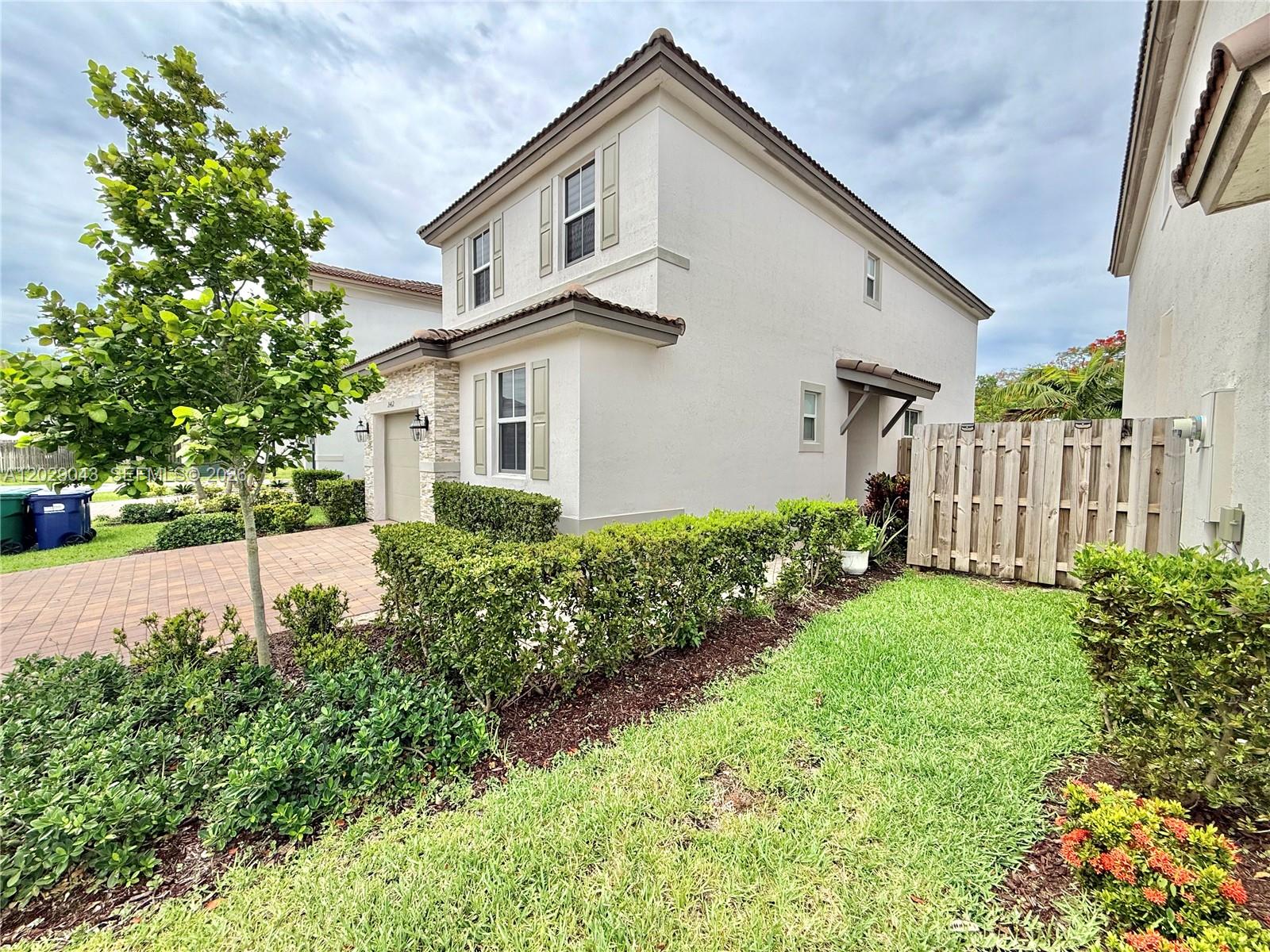 A two-story stucco house features a paved driveway, manicured hedges, and a wooden privacy fence — 2462 NW 131st Cir, Miami FL 33167, MIAMI, FL