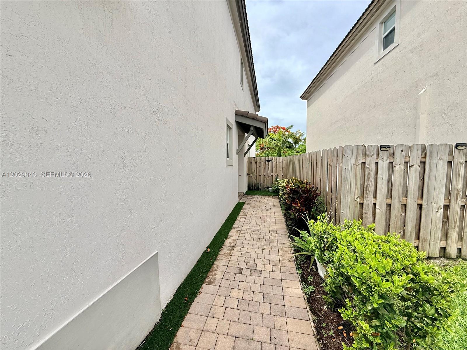A paved walkway runs between a white stucco house wall and a wooden privacy fence — 2462 NW 131st Cir, Miami FL 33167, MIAMI, FL
