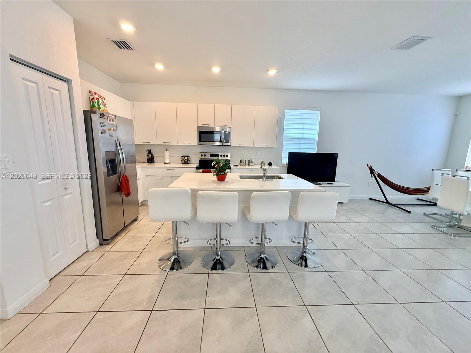 A modern kitchen features white cabinetry, a central island with bar seating, and tile flooring — 2462 NW 131st Cir, Miami FL 33167, MIAMI, FL