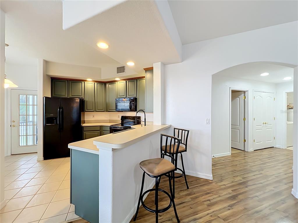 A kitchen with green cabinets, black appliances, and a breakfast bar overlooks a living area — 17308 PROMENADE DRIVE, CLERMONT, FL