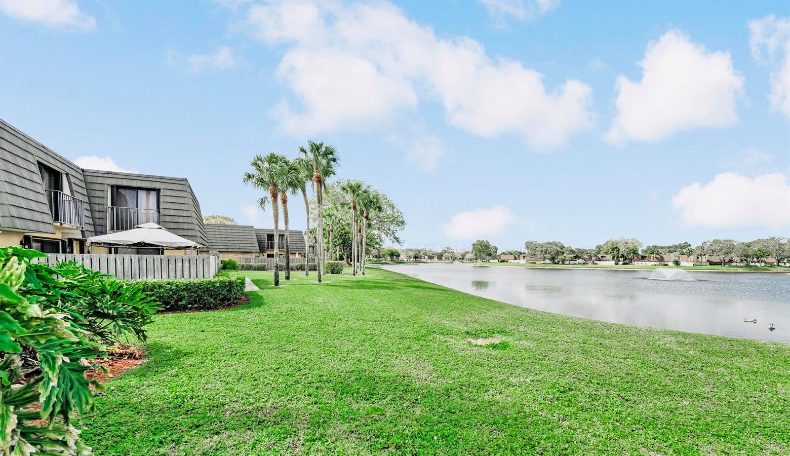 A grassy lawn leads to a lake beside a multi-story building with palm trees — 2439 24th Way # 2439, West Palm Beach FL 33407, WEST PALM BEACH, FL