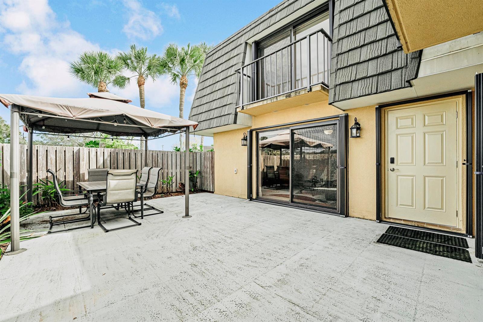 A patio with a gazebo, outdoor dining set, sliding glass door, and a beige entry door — 2439 24th Way # 2439, West Palm Beach FL 33407, WEST PALM BEACH, FL