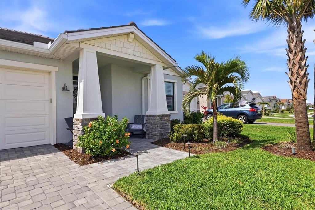 The exterior of a single-story house features a paved walkway, stone-based columns, and landscaping — 18645 MIDSUMMER PLACE, VENICE, FL