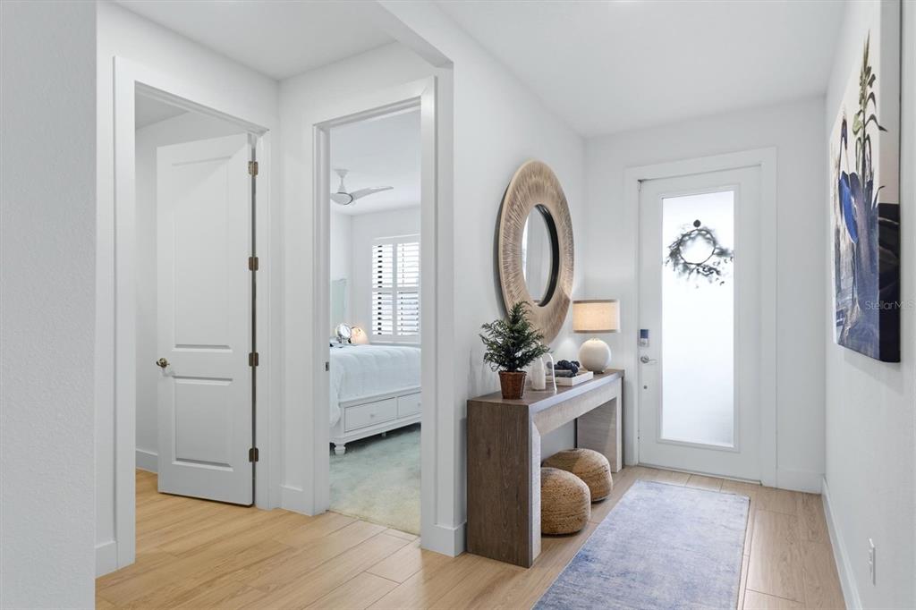 A bright entryway features light wood flooring, a console table, and a doorway to a bedroom — 18645 MIDSUMMER PLACE, VENICE, FL