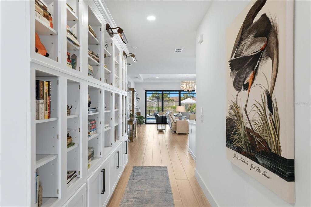 A hallway features built-in white bookshelves, a large bird print, and light wood flooring — 18645 MIDSUMMER PLACE, VENICE, FL