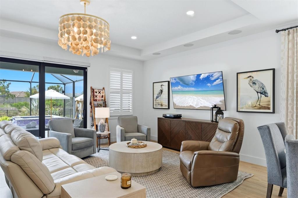 A living room features a shell chandelier, a television, and a view of a pool — 18645 MIDSUMMER PLACE, VENICE, FL