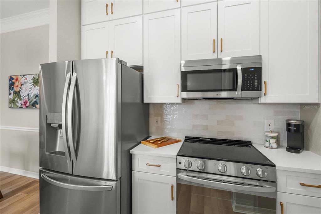 A kitchen features white cabinets, stainless steel appliances, and a light-colored tile backsplash — 5160 NORTHRIDGE ROAD UNIT 302, SARASOTA, FL