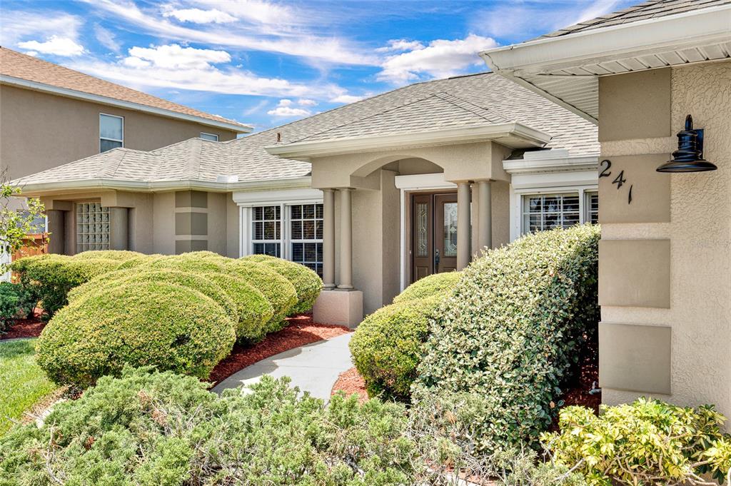 The exterior of a beige house features a covered entryway, manicured shrubs, and a walkway — 241 CORONA AVENUE, COCOA BEACH, FL
