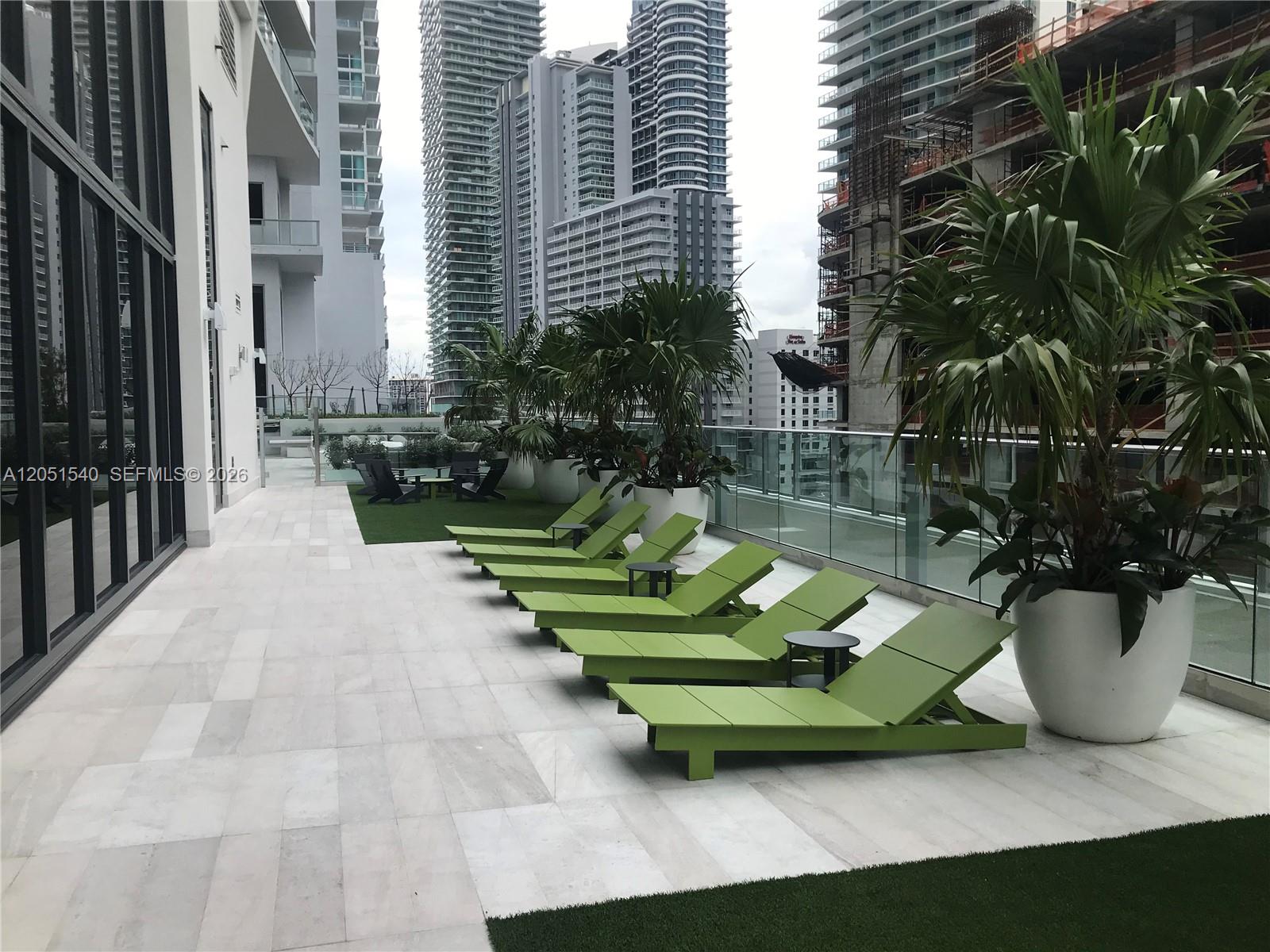 A row of green lounge chairs sits on a paved terrace with potted palm trees — 1010 Brickell Ave # 3309, Miami FL 33131, MIAMI, FL