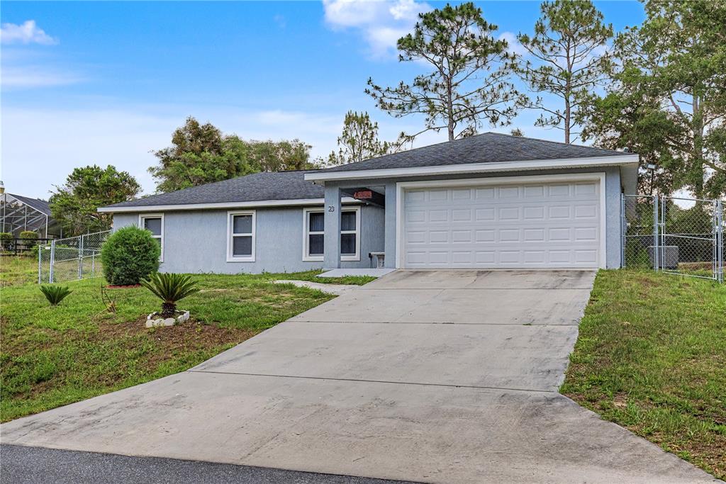 A single-story house with a gray stucco exterior, a concrete driveway, and a two-car garage — 23 JUNIPER TRAIL CIRCLE, OCALA, FL
