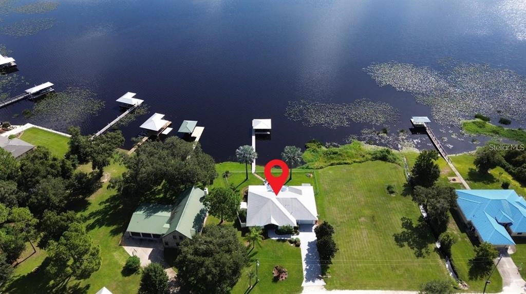 An aerial view shows a white house with a metal roof situated on a lakefront — 2608 PINE NEEDLE DRIVE, SEBRING, FL