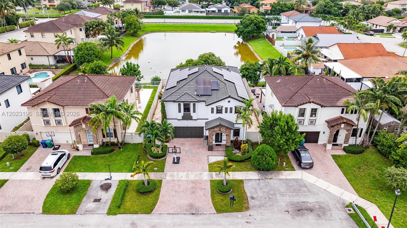 An aerial view shows three suburban houses with tiled roofs and driveways near a pond — 16125 SW 65th Ln, Miami FL 33193, MIAMI, FL