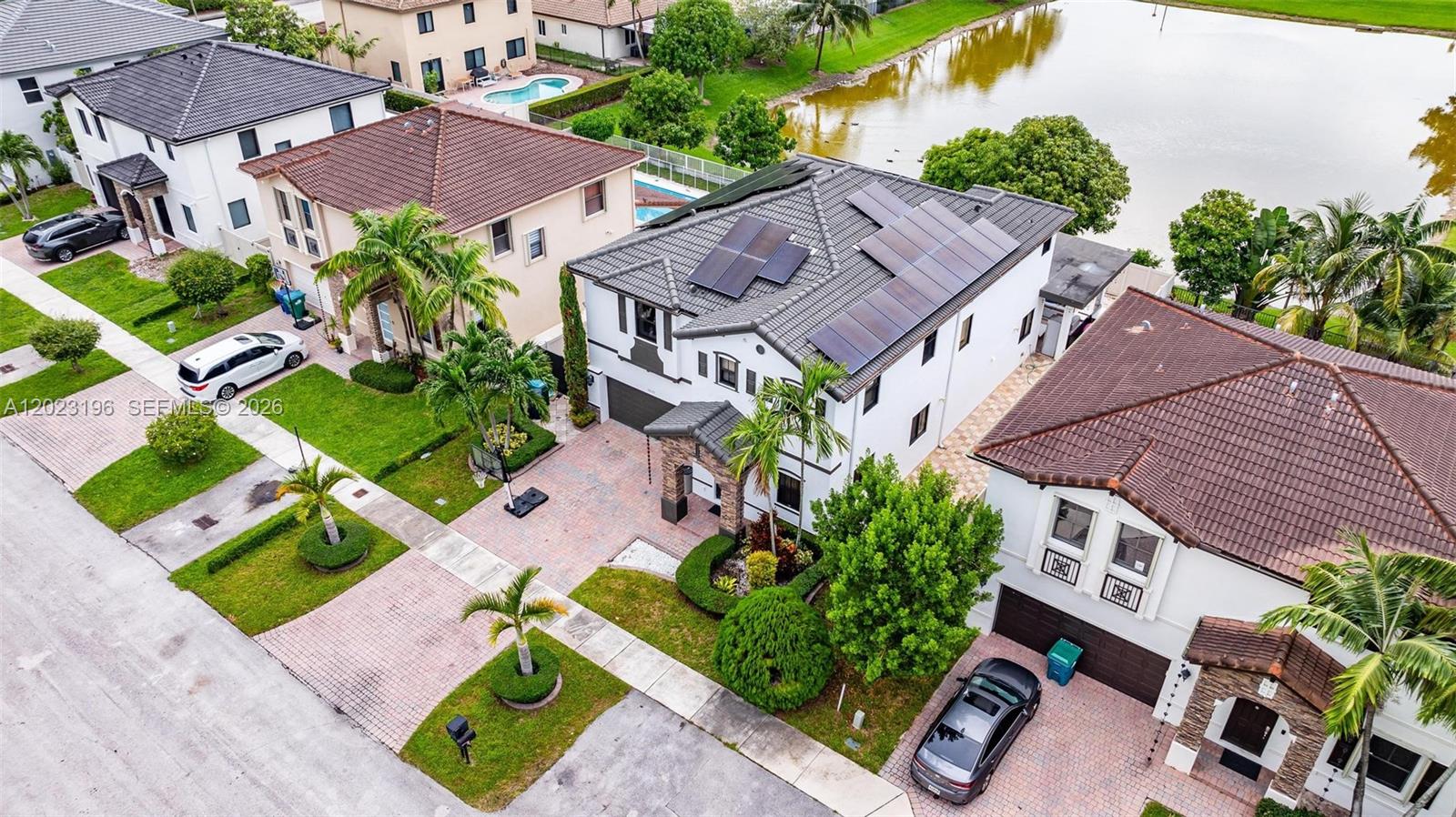 An aerial view shows suburban houses with tiled roofs, solar panels, and driveways near a lake — 16125 SW 65th Ln, Miami FL 33193, MIAMI, FL