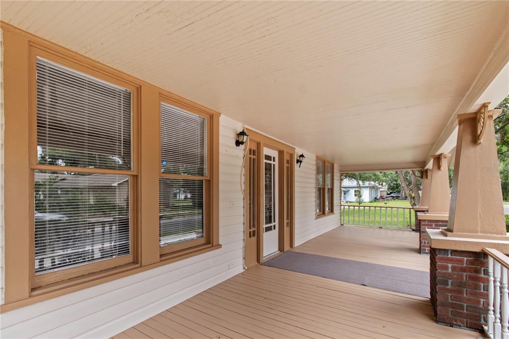 A covered front porch features light-colored wood flooring, brick columns, and white siding — 907 N CLARK STREET, PLANT CITY, FL