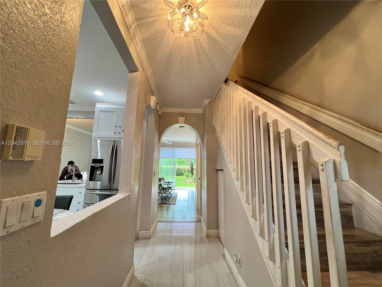 A hallway features a staircase with white railings, tile flooring, and an arched entryway — 8917 NW 54th St, Sunrise FL 33351, SUNRISE, FL