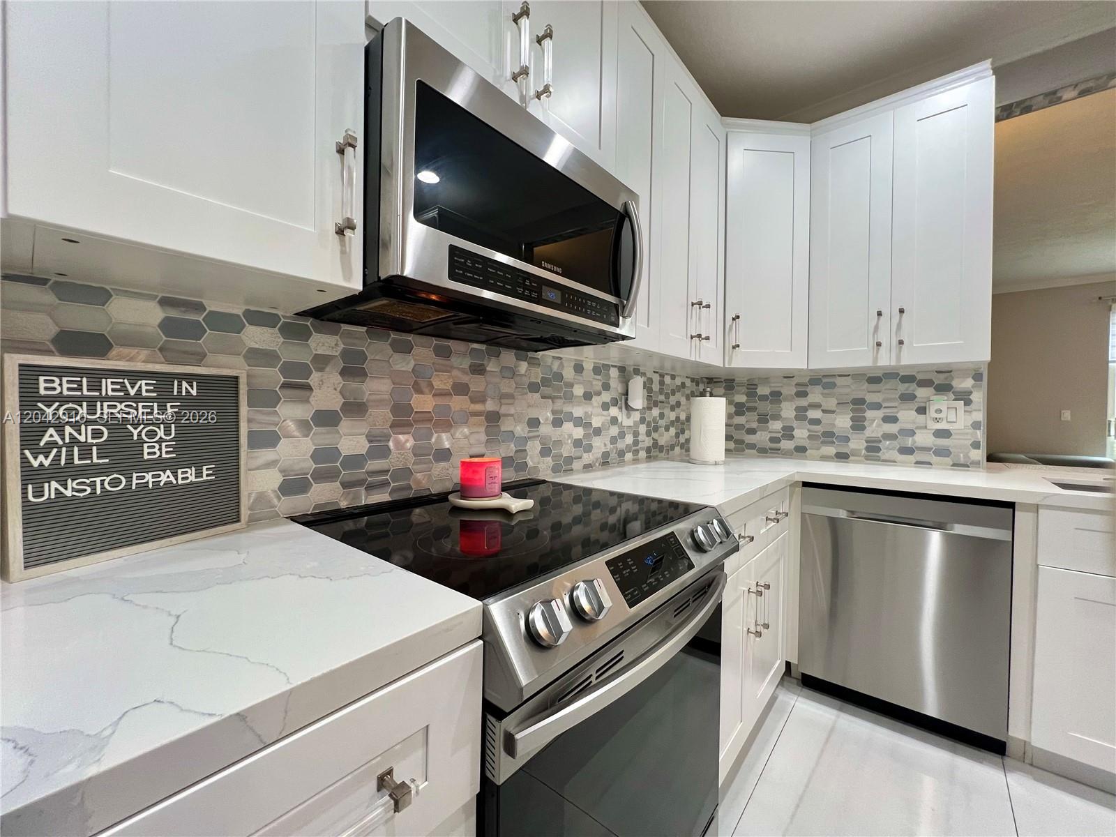A modern kitchen features white cabinets, stainless steel appliances, and a hexagonal tile backsplash — 8917 NW 54th St, Sunrise FL 33351, SUNRISE, FL