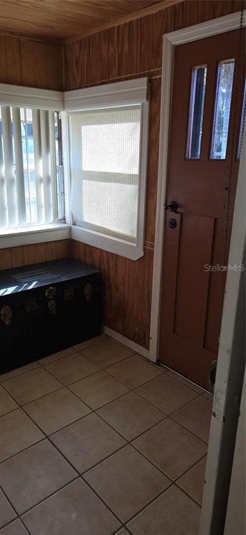 A small room with wood-paneled walls, tile flooring, a black storage chest, and a brown door — 315 VIRGINIA STREET, FROSTPROOF, FL