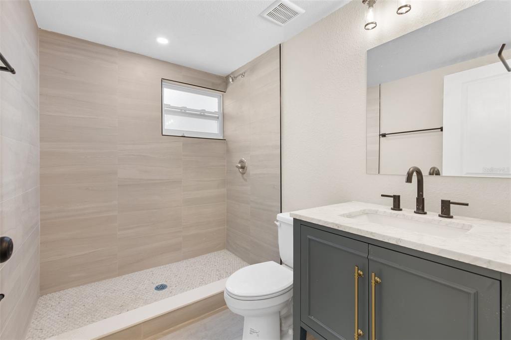 A bathroom features a walk-in shower with beige tile, a white toilet, and a gray vanity — 781 31ST AVENUE N, ST PETERSBURG, FL