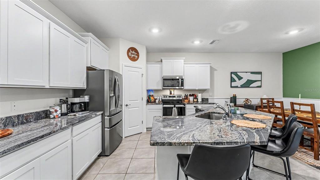 A kitchen features white cabinets, granite countertops, a stainless steel refrigerator, and a center island — 3817 STORMY THISTLE PLACE, PLANT CITY, FL