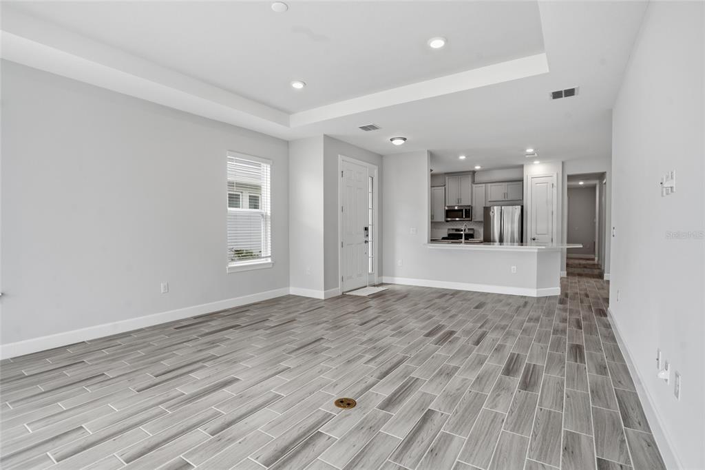 An open-concept living area features gray wood-look tile flooring, a tray ceiling, and a kitchen — 4718 GAROFALO ROAD, WESLEY CHAPEL, FL