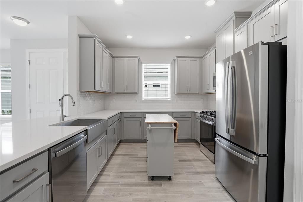A kitchen features gray cabinets, stainless steel appliances, a center island, and wood-look tile flooring — 4718 GAROFALO ROAD, WESLEY CHAPEL, FL