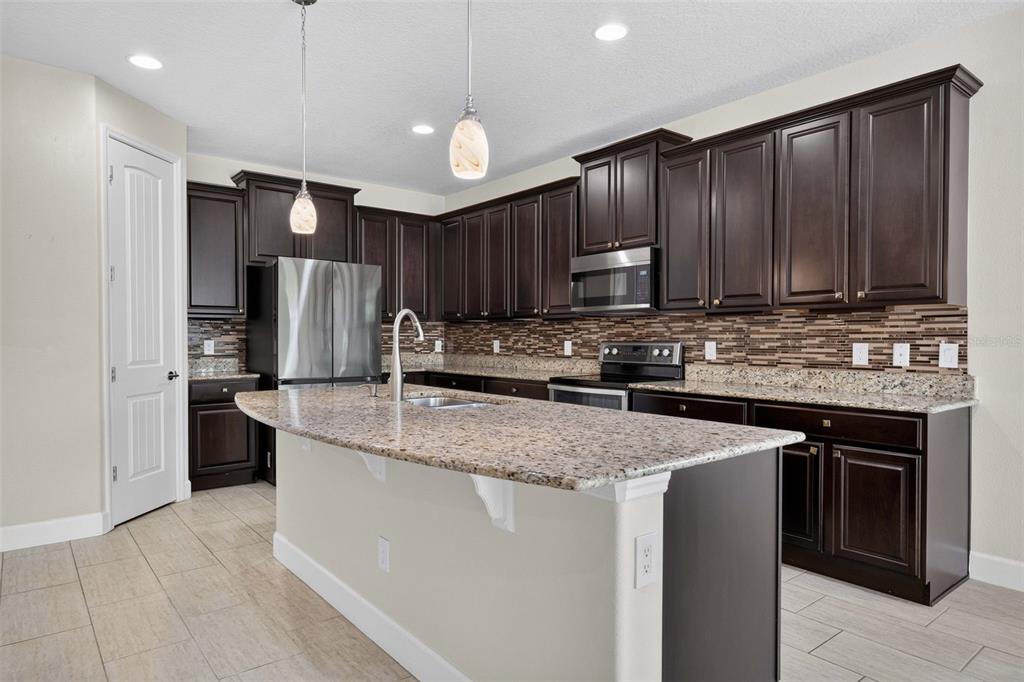 A kitchen features dark wood cabinets, granite countertops, a center island, and stainless steel appliances — 11812 PADUA LANE, ORLANDO, FL