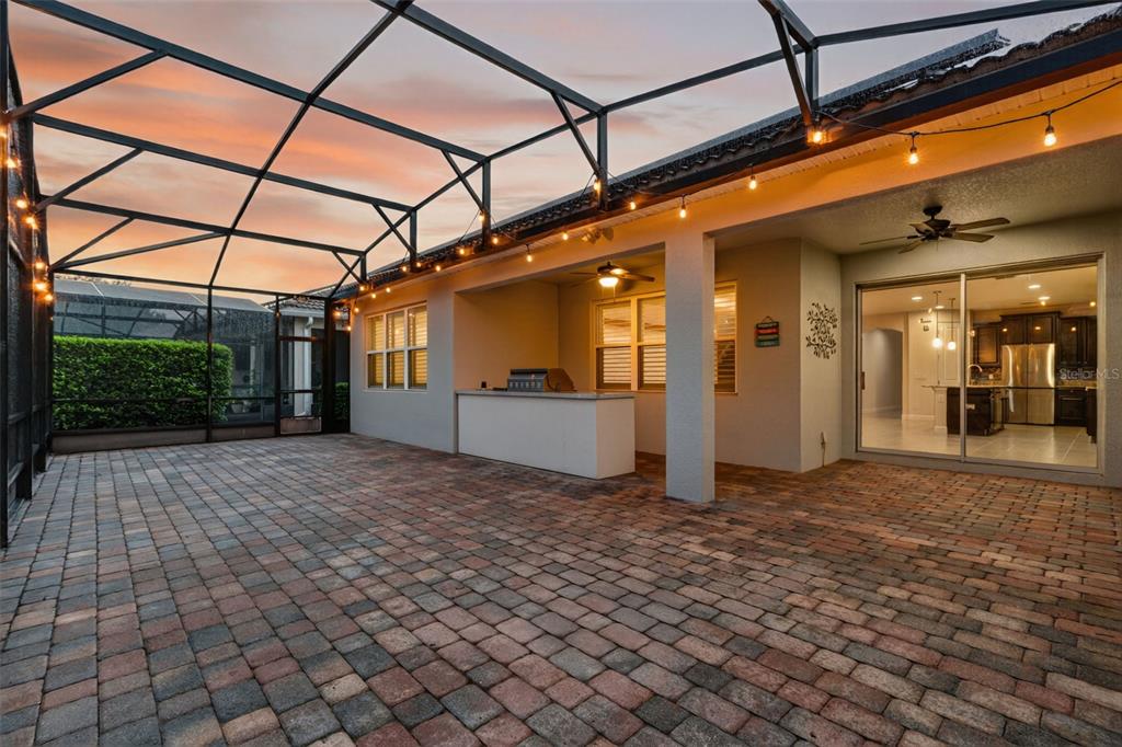 A covered patio with brick pavers, a built-in bar, and a screened-in enclosure at sunset — 11812 PADUA LANE, ORLANDO, FL