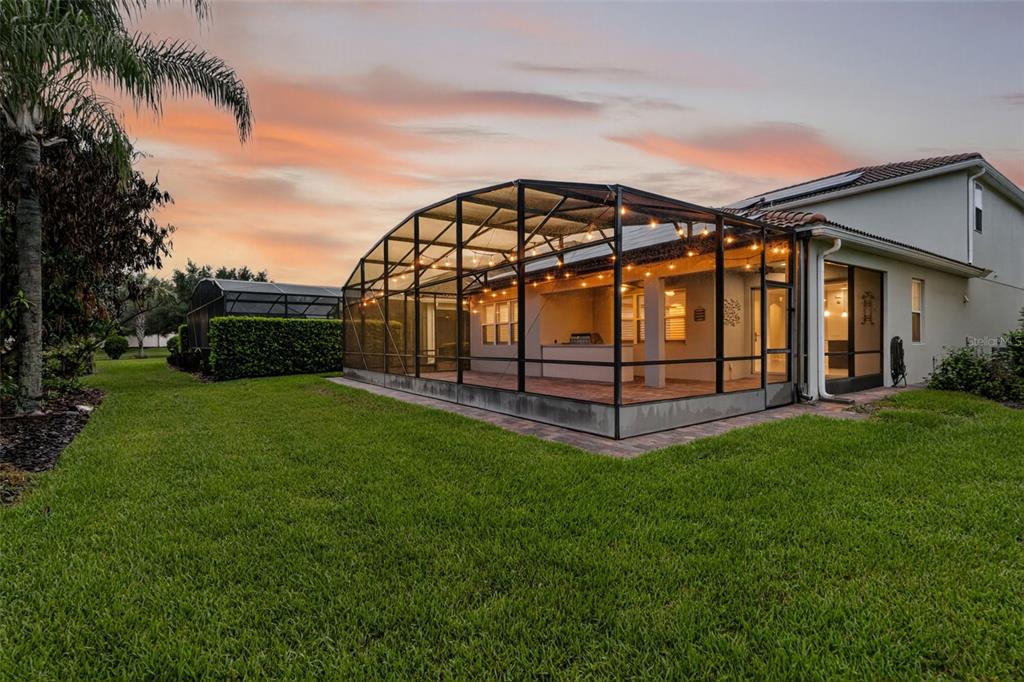 A screened-in patio with an outdoor kitchen sits beside a house in a grassy backyard — 11812 PADUA LANE, ORLANDO, FL