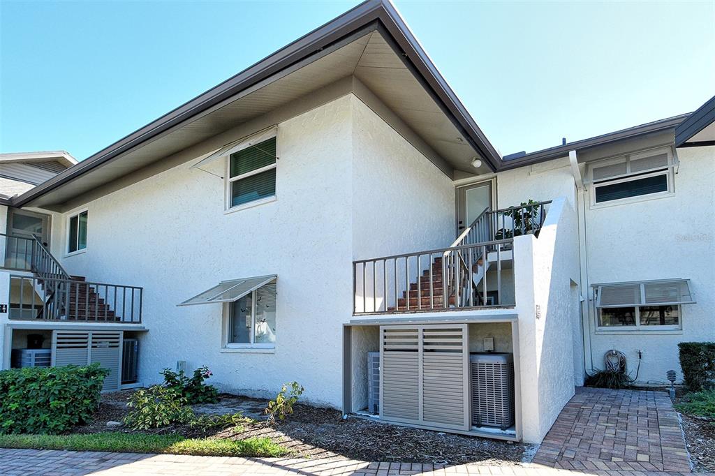 Exterior view of a two-story white stucco building with metal staircases and ground-level utility enclosures — 4234 GULF OF MEXICO DRIVE UNIT E2, LONGBOAT KEY, FL