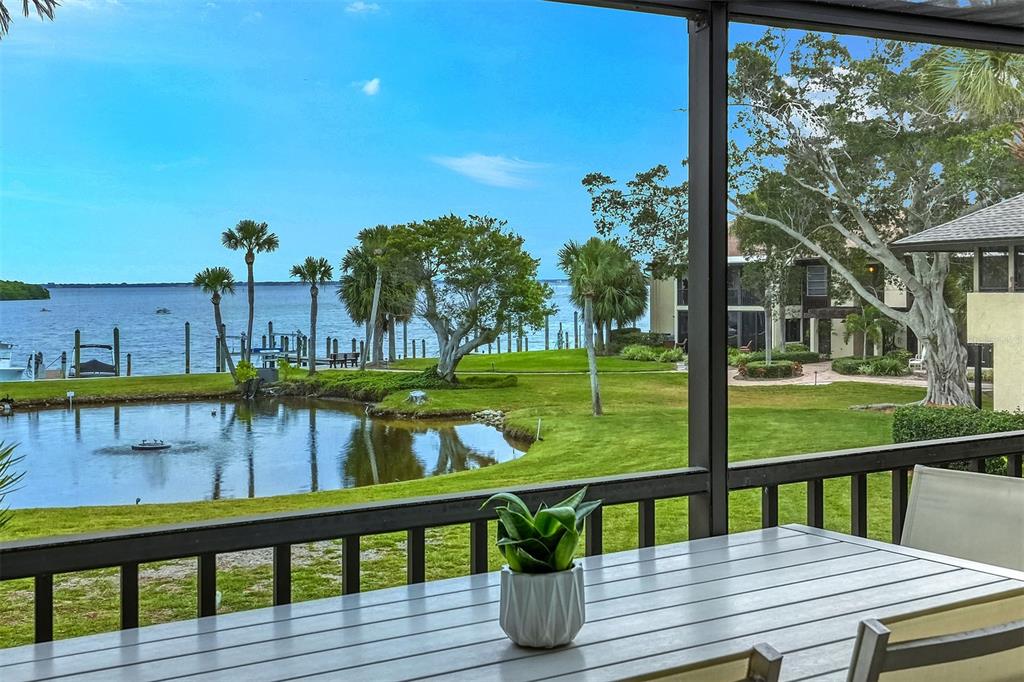 A screened-in patio overlooks a small pond, green lawn, and a large body of water — 4234 GULF OF MEXICO DRIVE UNIT E2, LONGBOAT KEY, FL