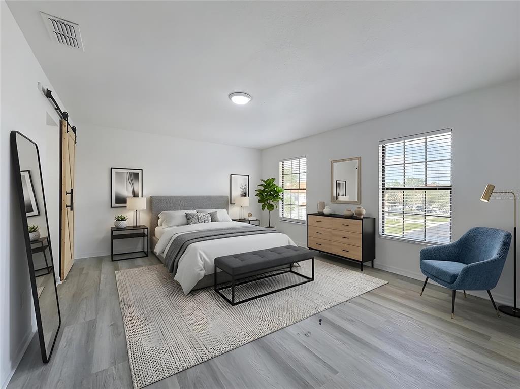 A bedroom with light wood-look flooring, a gray upholstered bed, and a blue accent chair — 16710 CARIBBEAN BREEZE WAY, CLERMONT, FL